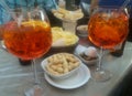 Two glasses of aperol spritz with hors d`oeuvres of green olives, chips and peanuts Royalty Free Stock Photo