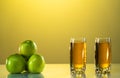 Two glasses of apple juice with green apples in the sunset background. yellow background. Reflected surface. Summer day Royalty Free Stock Photo