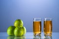 Two glasses of apple juice with green apples in theblue background. yellow background. Reflected surface. Summer day Royalty Free Stock Photo