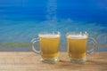 Two glasses of beer on a beach on wooden table with the sea water background on a sunny summer day, closeup Royalty Free Stock Photo