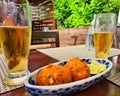 two glasses of beer being drank with a portion of fried cod fritters in a leafy restaurant during summer