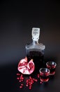 Two glasses with bright red liqueur and a glass bottle on a black background, next to a ripe pomegranate and fruit seeds Royalty Free Stock Photo