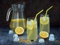 Two glasses and carafe of cold homemade lemonade with lemon slices, ice cubes, brown sugar, yellow straws