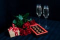 Two glasses with champagne and a bouquet of red roses and candies on the black background Royalty Free Stock Photo