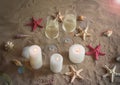 Two glasses of champagne, candles, shells and starfishes on sand beach.
