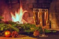 Two glasses of champagne, decorations, Christmas tree branches and a candle on a wooden table in front of a burning fireplace Royalty Free Stock Photo