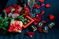 Two glasses of champagne, red roses, petals, gift box with red ribbon, chocolates and wooden love words on a black background Royalty Free Stock Photo