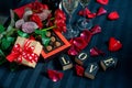 Two glasses of champagne, red roses, petals, gift box with red ribbon, chocolates and wooden love words on a black background Royalty Free Stock Photo