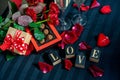 Two glasses of champagne, red roses, petals, gift box with red ribbon, chocolates and wooden love words on a black background Royalty Free Stock Photo