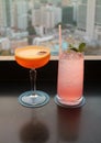 Two glasses of cocktail on the rooftop bar`s table with blurry aerial urban view in background