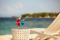 Two glasses with cocktails on table near beach bench or deck chair with blue ocean and white sand on background Royalty Free Stock Photo