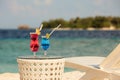Two glasses with cocktails on table near beach bench or deck chair with blue ocean and white sand on background Royalty Free Stock Photo