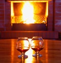 Two glasses of cognac on the old brick fireplace with bright fire Royalty Free Stock Photo