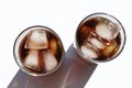 Two glasses of cola with ice cubes on white table. Top view, copy space. Hard light, shadow.  Refreshing summer drink Royalty Free Stock Photo