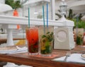 Two glasses of cold mojitos and an iced strawberry cocktail sit on a table on the cafe`s summer veranda. Glasses with a tube cover Royalty Free Stock Photo