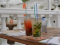 Two glasses of cold mojitos and an iced strawberry cocktail sit on a table on the cafe`s summer veranda. Glasses with a tube cover Royalty Free Stock Photo