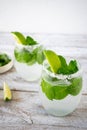 Two glasses with cool drinks with lime and mint stand on a wooden table.