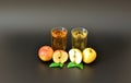 Two glasses with different fruit juices on a black background, next to pieces of ripe red and yellow apples with leaves Royalty Free Stock Photo