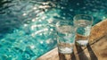 Two glasses filled with fresh water are placed on top of a wooden table next to a clear pool. Royalty Free Stock Photo