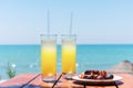 Two glasses of fresh tropical fruit juice on the beach, and a plate with grapes and watermelon on the table, against the sea. Holi Royalty Free Stock Photo