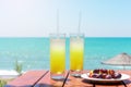 Two glasses of fresh tropical fruit juice on the beach, and a plate with grapes and watermelon on the table, against the sea. Holi Royalty Free Stock Photo