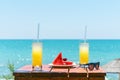 Two glasses of fresh tropical fruit juice on the beach, and a plate with grapes and watermelon on the table, against the sea. Holi Royalty Free Stock Photo