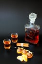 Two glasses and a glass bottle of cognac with tangerine, chocolates and cinnamon on a black background Royalty Free Stock Photo