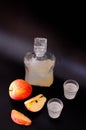 Two glasses and a glass decanter of Calvados, next to it are slices of ripe apple on a black background Royalty Free Stock Photo