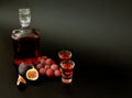 Two glasses and a glass decanter with homemade liqueur on a black background, next to pieces of ripe figs and a bunch of red Royalty Free Stock Photo