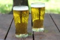 Two glasses of golden cold beer on wooden table, outdoor. With copy space, close up.