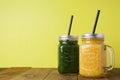 Two glasses with green and yellow detox smoothie with straws. Spinach and pumpkin smoothie on wooden table and yellow backgraund