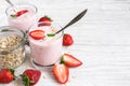 Two glasses of healthy strawberry yogurt with fresh berries, oats spoon and mint on white wooden table