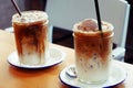 Two glasses of iced coffee, one topped with ice cream, each glass placed on white plate and both placed on wooden table Royalty Free Stock Photo