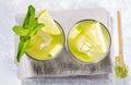 Two glasses of iced green matcha tea with lime, ice, fresh mint and wooden spoon of powder on grey napkin on grey Royalty Free Stock Photo