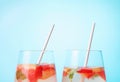 Two glasses with iced tea with pieces of strawberry and grapefruit. Summer refreshing drink, front view.