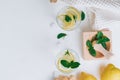 Two glasses with lemonade. Ingredients ginger, lemon, mint, ice on white surface. Mortar, pestle. Flat lay. Copy space Royalty Free Stock Photo