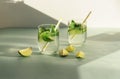 Two glasses of lemonade with straw and lime slices on blue table. Cold refreshing drinks against white wall in sunlight Royalty Free Stock Photo