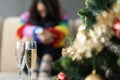 Two glasses near decorated christmas tree and sad woman sitting alone