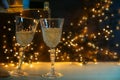 Two glasses are poured with champagne for a New Year party toast, golden bokeh lights in the dark background, copy space, selected Royalty Free Stock Photo