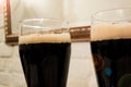 Two glasses poured with dark beer or soft drink with foam head. Close up image against white brick wall in bar or pub Royalty Free Stock Photo
