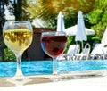 Two glasses of red and white wine are placed by the pool. The concept of a pleasant stay. Royalty Free Stock Photo