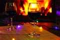 Two glasses of red wine against the background of a burning fireplace in hard reflective lighting. Romantic relaxed dinner by the