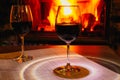 Two glasses of red wine against the background of a burning fireplace in hard reflective lighting. Romantic relaxed dinner by the
