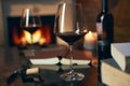 Two glasses of red wine with book and candle on table at home, fireplace in the background. Royalty Free Stock Photo