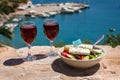 Two glasses of red wine and bowl of greek salad with greek flag on by the sea view, summer greek holidays concept. Royalty Free Stock Photo