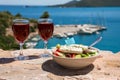 Two glasses of red wine and bowl of greek salad with greek flag on by the sea view, summer greek holidays concept. Royalty Free Stock Photo