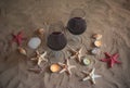 Two glasses of red wine, burning candles, seashells and starfishes on sand beach. Royalty Free Stock Photo