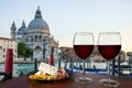 Two glasses of red wine with charcuterie assortment on gondolas and Santa Maria della Salute. Glass of red wine with different