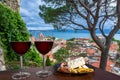 Two glasses of red wine with charcuterie assortment with view of Croatian town Omis with red roofs and blue sea. Glass of red wine