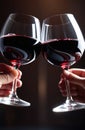 Two glasses of red wine clinking. Cheers with wineglasses, close up on hands. Celebration concept